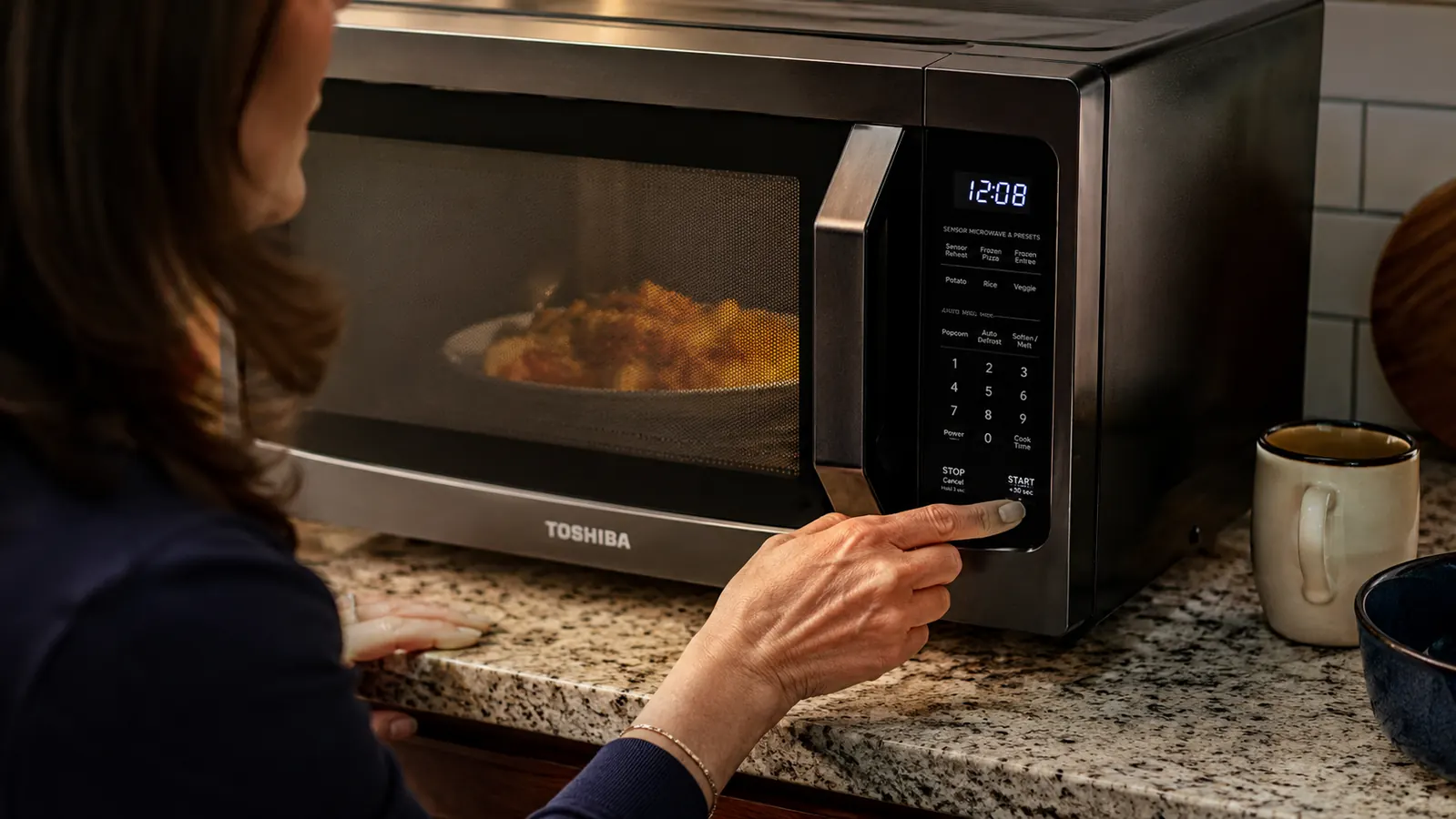 Hand pressing the auto menu button on the Toshiba microwave control panel to reheat a plate of food