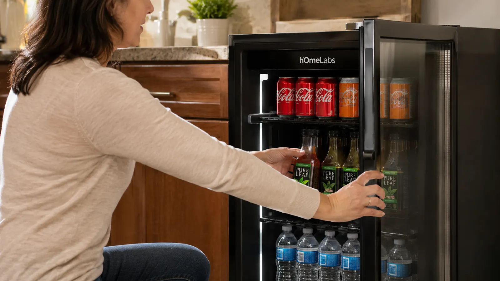 Hand opening the glass door of the hOmeLabs beverage fridge to restock soda cans on the adjustable shelves