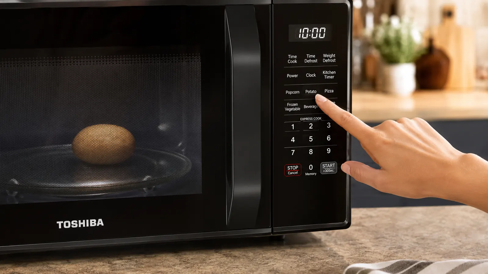 Hand pressing the potato auto-menu button on the Toshiba microwave control panel with a small potato visible on the turntable